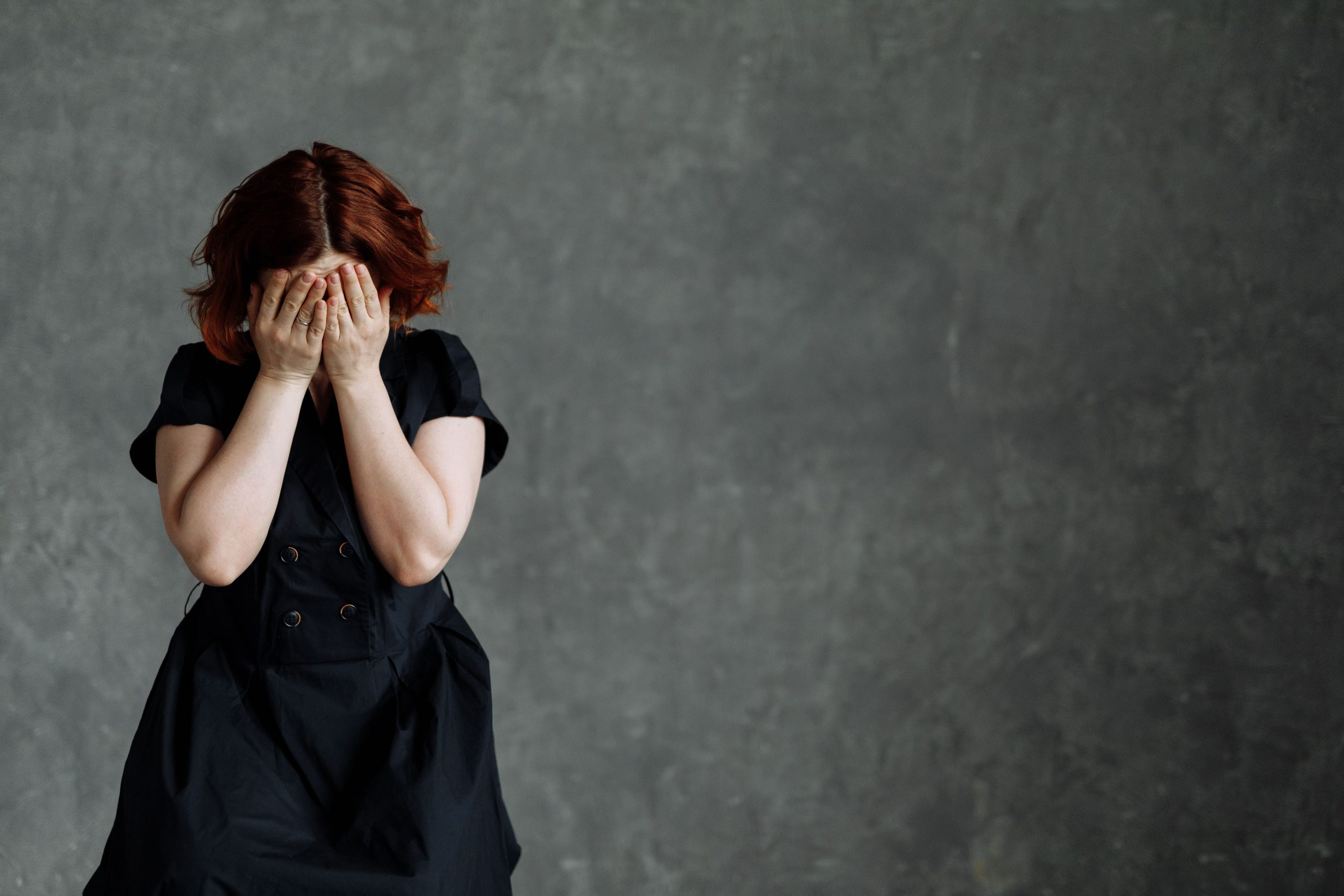 A woman in a black dress expressing emotion against a concrete backdrop, highlighting themes of sadness and stress.